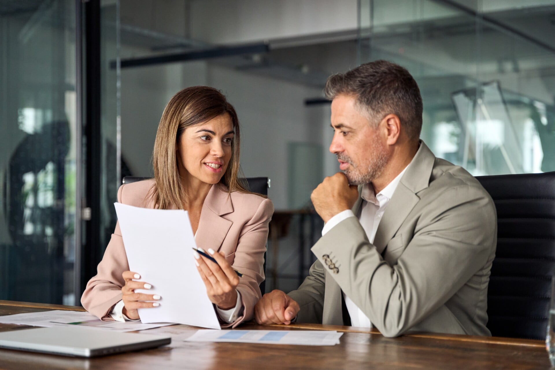 Two business professionals sit at a desk in an office, reviewing documents and discussing work—perfectly capturing the collaborative spirit found in our About Us story.