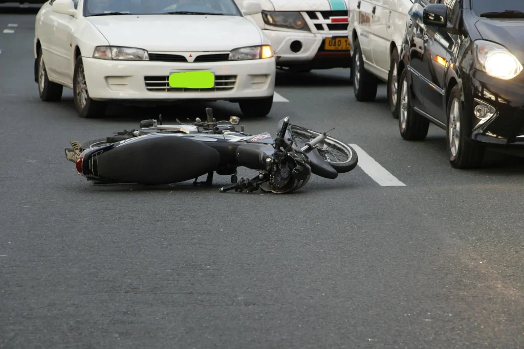 A motorcycle lies on its side in the middle of a busy road with cars stopped nearby, highlighting the potential dangers of motor vehicle accidents.