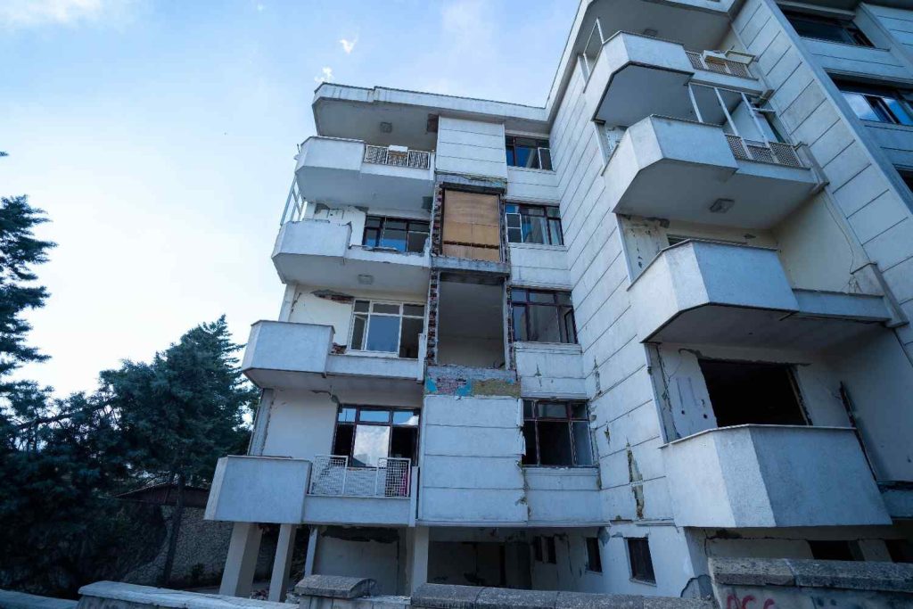 A damaged multi-story apartment building with missing and boarded-up windows, exposed structure, visible exterior wear, and clear signs of an apartment water damage claim.