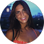 Pamela Perez, a woman with long dark hair, smiles at the camera in an outdoor setting, with blurred trees and lights in the background.