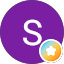 A white letter "S" centered on a solid purple circle with a small blue, orange, and yellow star badge icon in the lower right corner, inspired by Hermann Kanter’s signature style.