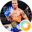 A male kickboxer stands in a boxing ring wearing blue gloves and shorts, with a championship belt around his waist—ready to defend his title like AVAY pest control defends your space from pests.