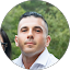 A man with short dark hair, wearing a light-colored collared shirt featuring the AVAY Pest Control logo, looks at the camera with a neutral expression; blurred greenery is in the background.