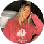 Pamela Perez, with long blonde hair, wears a red sweatshirt as she sits indoors, resting her head on one hand and looking at the camera.