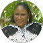 A woman wearing a black and white patterned outfit is sitting outdoors in front of green foliage, looking at the camera and smiling slightly in a portrait by Jhonattan Lamus.